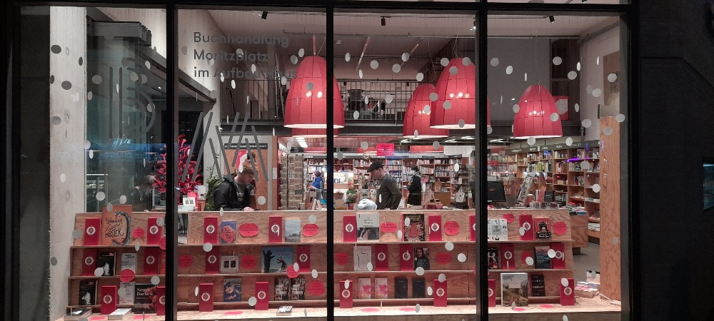 Schaufenster der Buchhandlung Moritzplatz, innen Licht, außen Dunkelheit, weihnachtlich geschmückt mit Schneeflocken aus Papier