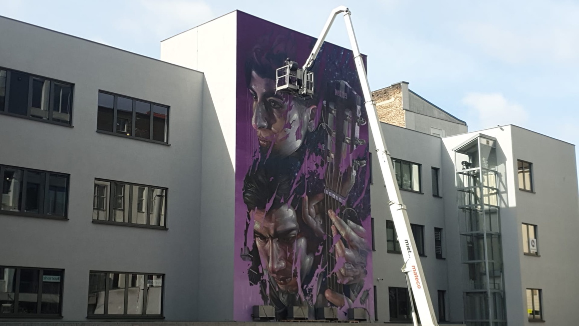 Kran mit Korb vor Graffito, das zwei überlebensgroße Gesichter zeigt