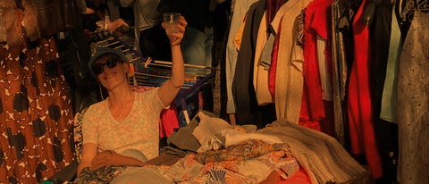 junge Frau im Sommer-Abendlicht sitzt inmitten eines vollen Trödelmarktstandes mit Kleidung
