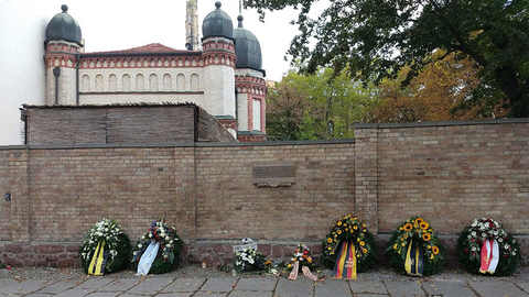 an einer Mauer liegen mehrere Blumenkränze zum Gedenken