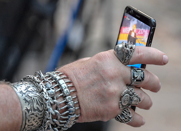 Hand mit vielen schweren silbernen Ringen und Armbändern hält Handy