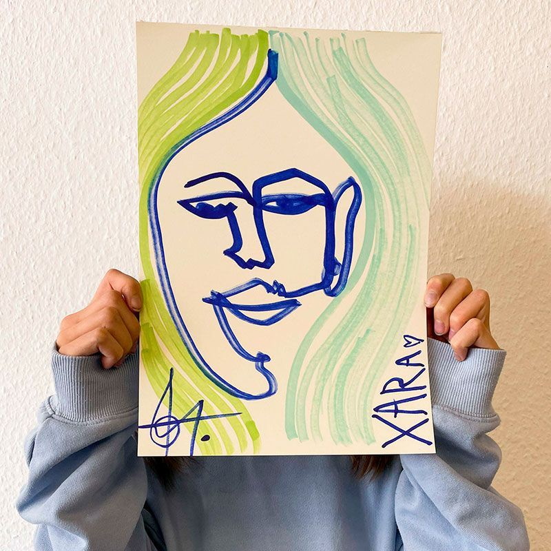 ein Mensch hält sich eine Blindzeichnung eines Gesichts mit dicken Linien vor das Gesicht