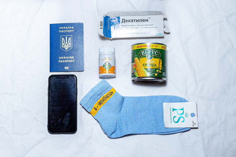 Dinge angeordnet auf einem weißen Tuch, neue hellblaue Socken, Handy, Reisepass, eine Dose Mais, Tabletten
