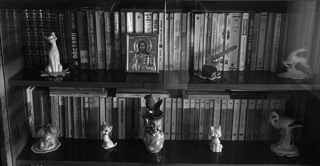 schwarz-weiß Foto, zwei voll gestellte Böden eines Bücherregals, vor den Büchern kleine Deko-Objekte