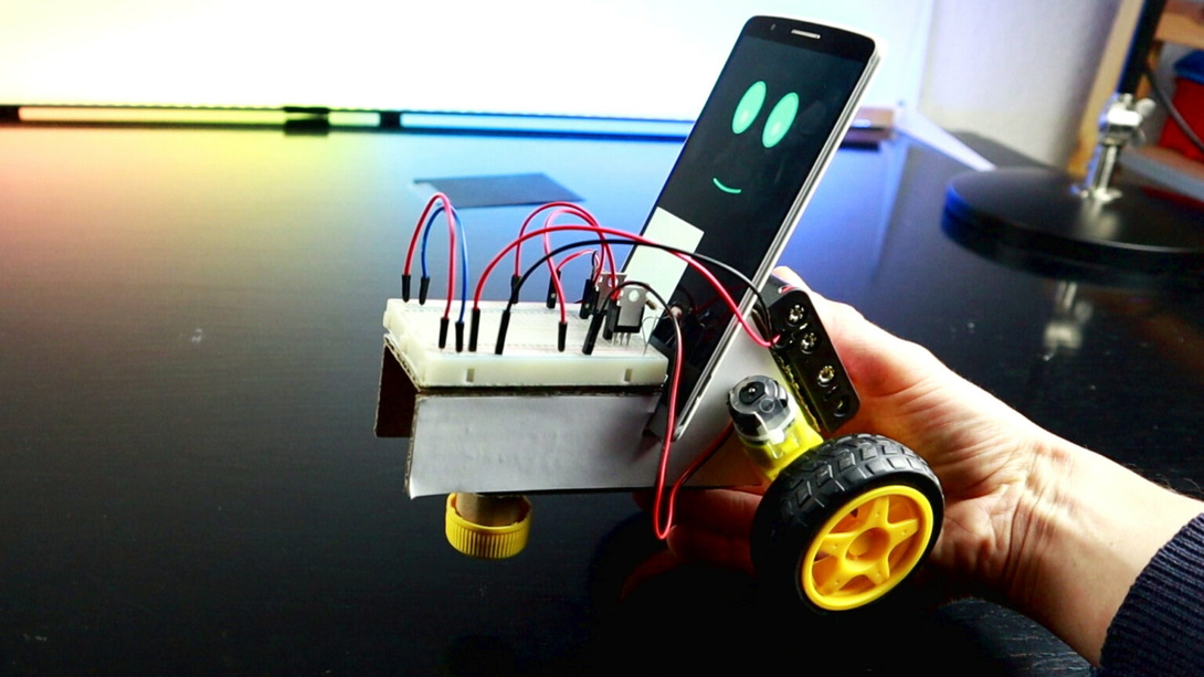 selbstgebastelter, kleiner Roboter, wie ein Auto, darin steckt ein Handy mit zwei Lichtpunkten wie ein Gesicht