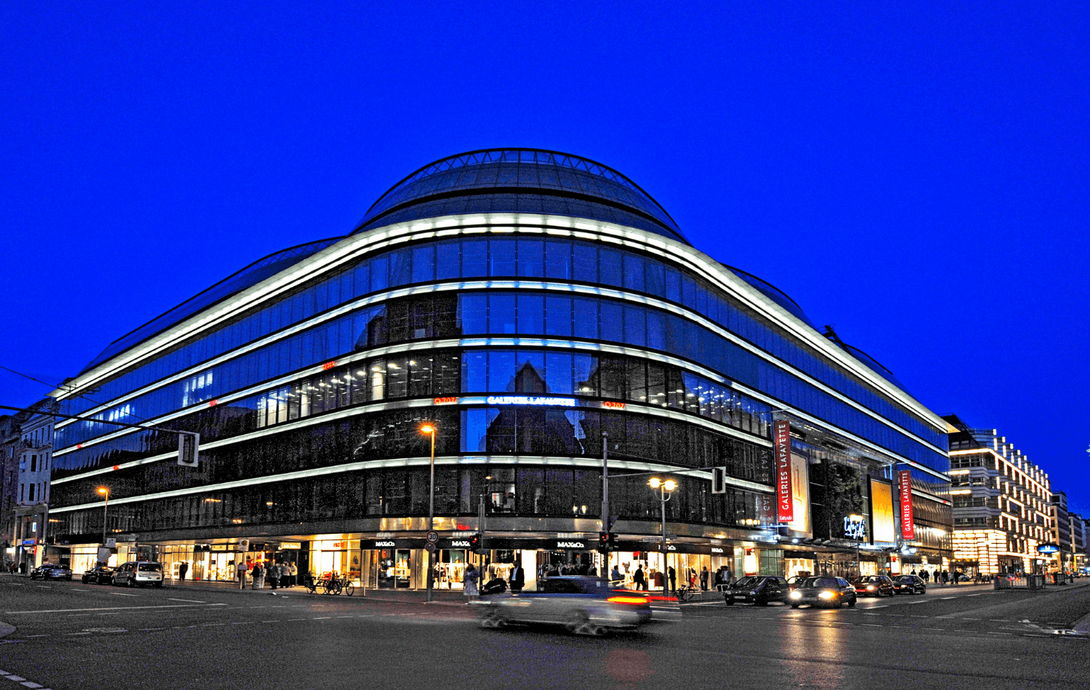 ein sehr großes, verspiegeltes Haus über Eck gebaut, beleuchtet, vor Nachthimmel fotografiert, deutlich bearbeitetes Foto