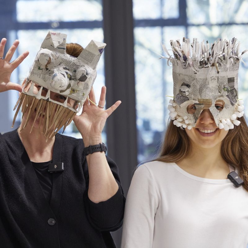 zwei junge Frauen mit aufwendig gebastelten Pappmasken auf dem Kopf
