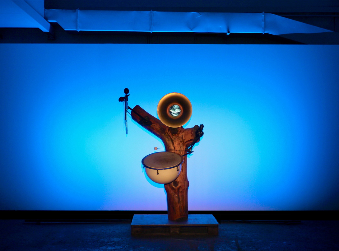 Skulptur aus einem Baumstamm mit Instrumenten, vor blauem Hintergrund