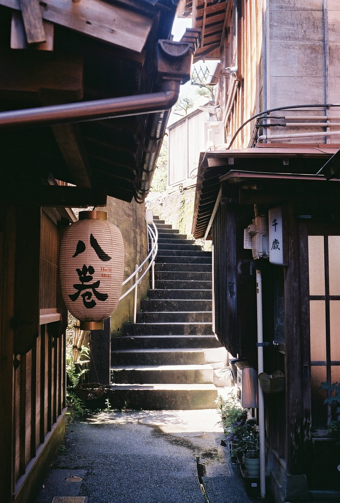 Blick durch eine Gasse, in der links eine Papierlampe mit asiatischen Schriftzeichen hängt, auf eine Treppe