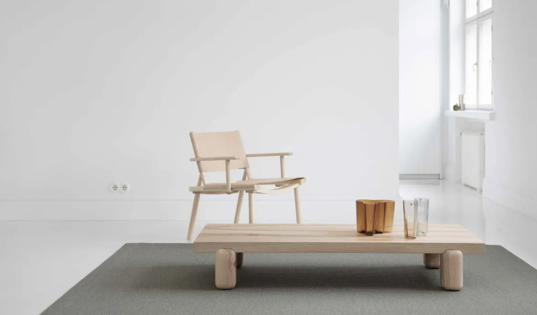 heller, luftiger Raum mit einem hellen Holzstuhl an einem Holz-Couchtisch, der auf einem dunklen Teppich steht