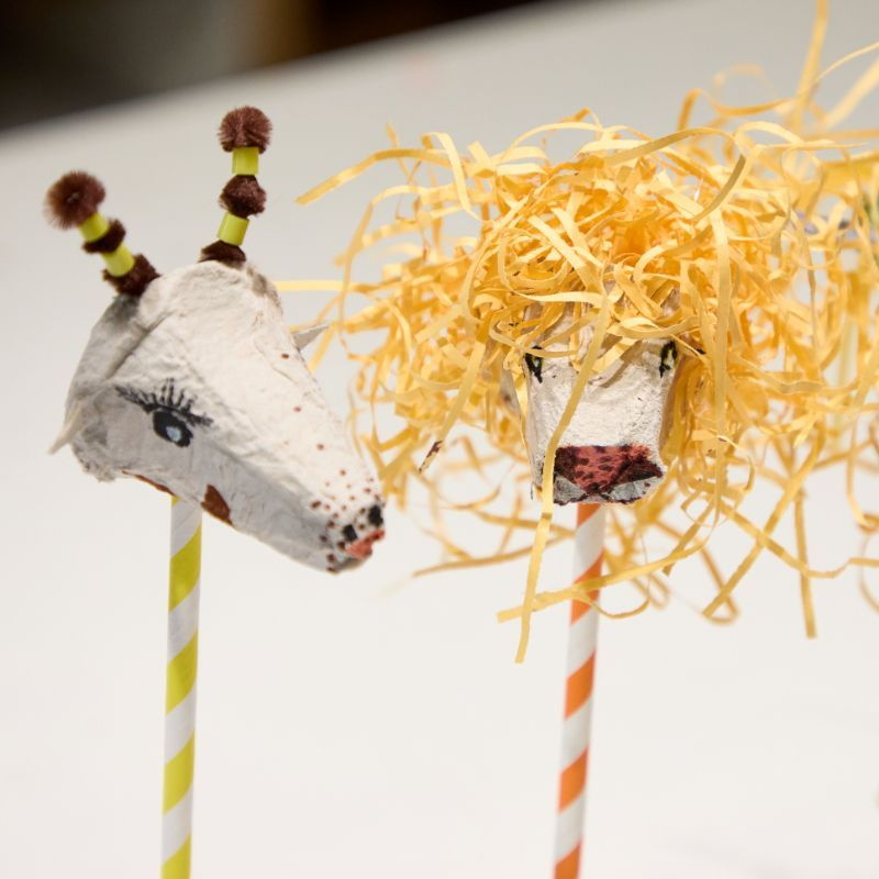 Tierköpfe aus den spitzen Teilen von Eierkartons, auf Strohhalmen, einer mit hochstehenden Ohren und einer mit Wuschelmähne aus Papierhalmen