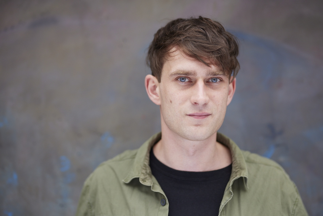 junger Mann in hellgrünem Hemd vor grauer Wand