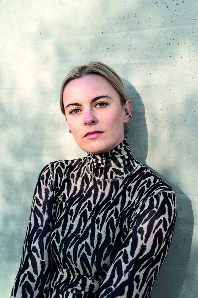 Porträt einer jungen blonden Frau in schwarz gemustertem Oberteil, Haare zurückgebundenl