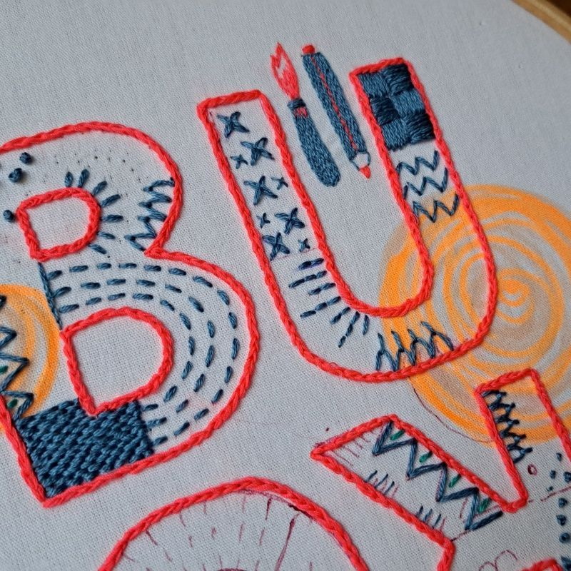 Nahaufnahme von gestickten Buchstaben, Kontur rot, mit unterschiedlichen blauen Mustern angefüllt