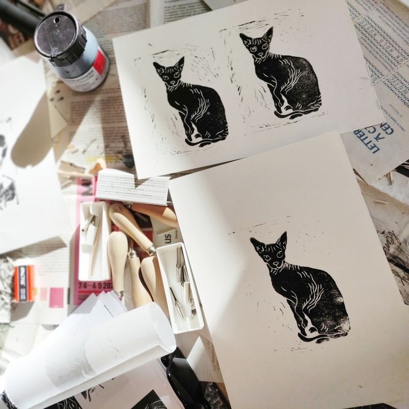 2 weiße Blätter, bedruckt mit jeweils einer bzw zwei schwarzen Katzen, darunter und daneben liegt Arbeitsmaterial