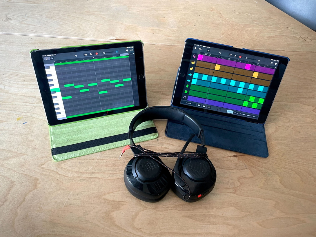 zwei aufgeklappte Laptops mit Grafiken auf den Bildschirmen, in der Mitte liegt ein Paar schwarze Kopfhörer