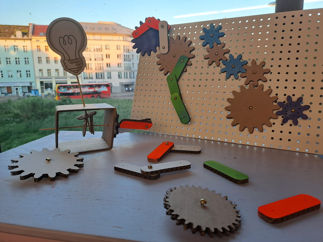 verschieden große Zahnräder aus Press-Span auf einem Tisch, im Hintergrund der Berliner Moritzplatz