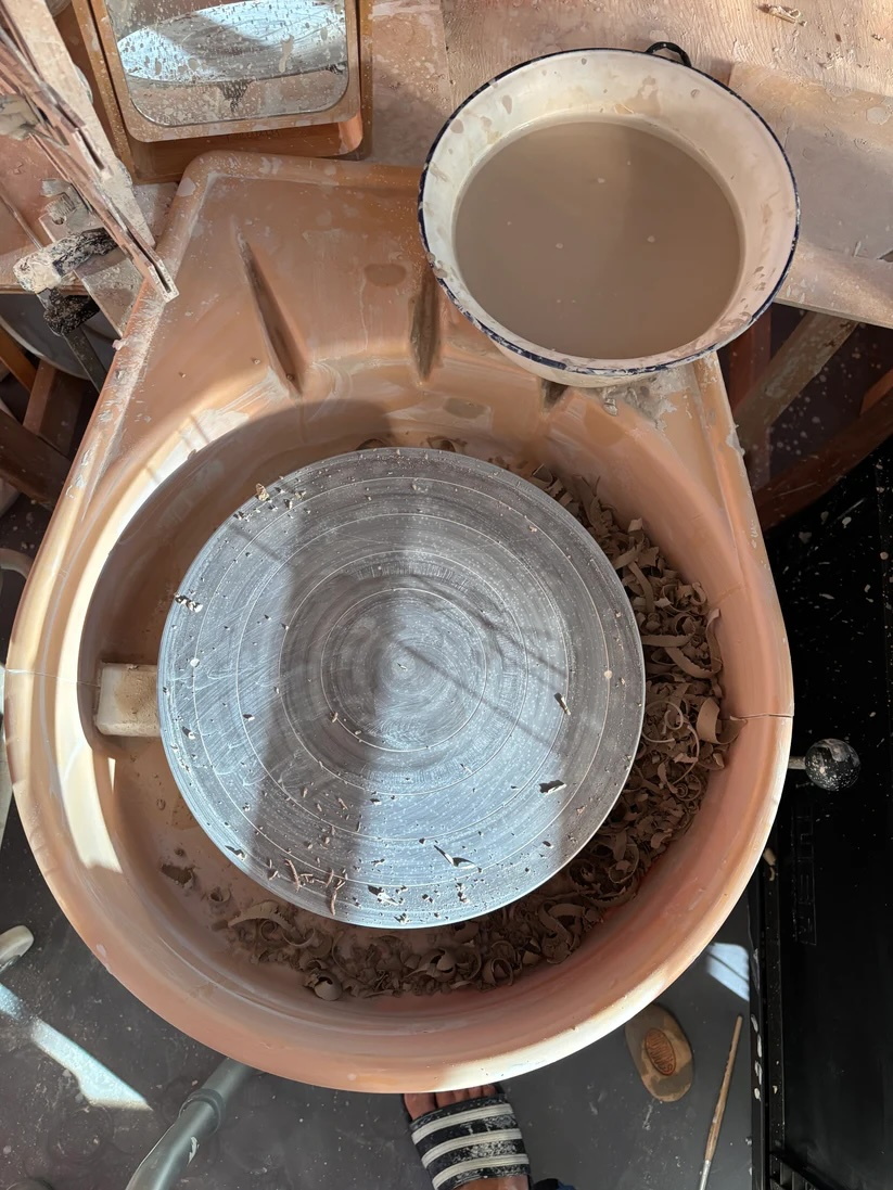 Ton Drehscheibe von oben fotografiert, daneben eine Emaille Schüssel mit trübem Wasser