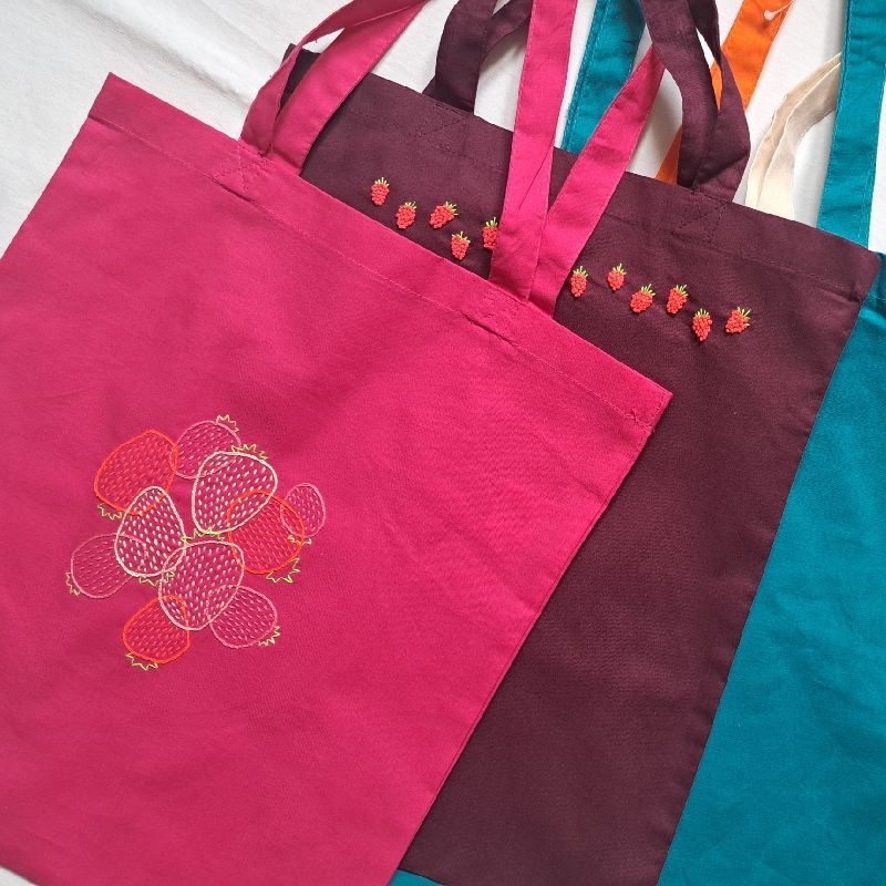übereinanderliegende Stoffbeutel in rosa, weinrot und türkisblau, individuell bestickt