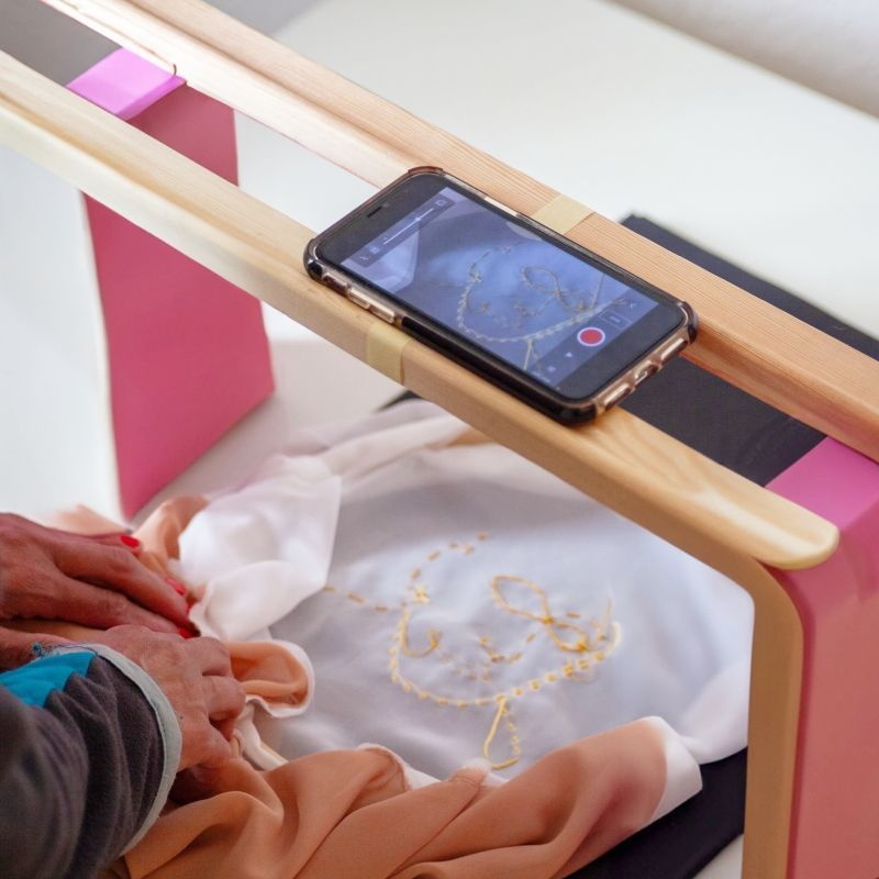 Handy liegt auf zwei Holzleisten, darunter ein besticktes Tuch, zwei Hände, die den Stoff anordnen