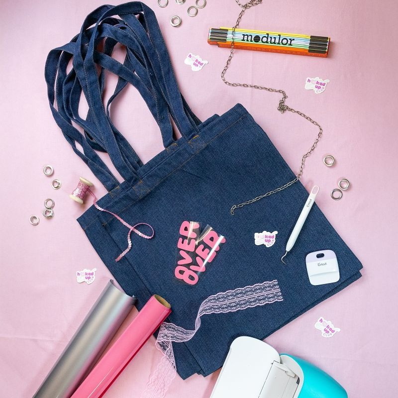 Jeanstasche, die voller Gestaltungsmaterial liegt, Zollstock, Papierrollen, Bänder, Nadeln etc.