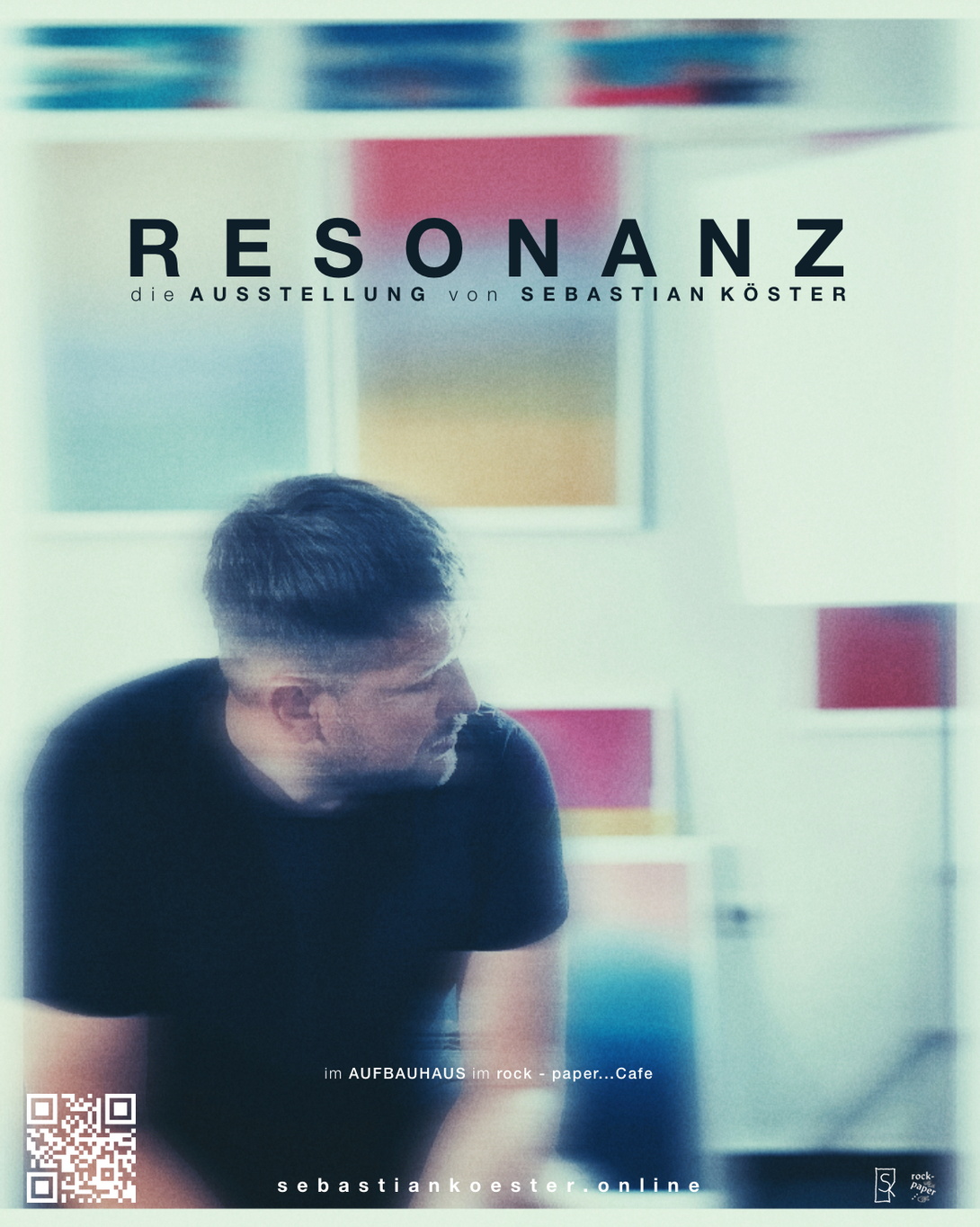 unscharfe Aufnahme eines kurzhaarigen Mannes im schwarzen T-Shirt vor bunten Bildern an einer hellen Wand 