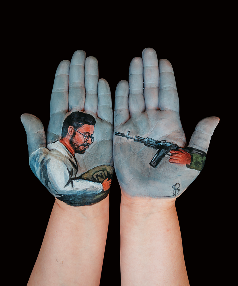 zwei Handflächen, in die ein Bild gemalt wurde, ein Maschinengewehr ist auf einen Mann mit kurzen dunklen Haaren und Brille in einem weißen Hemd gerichtet