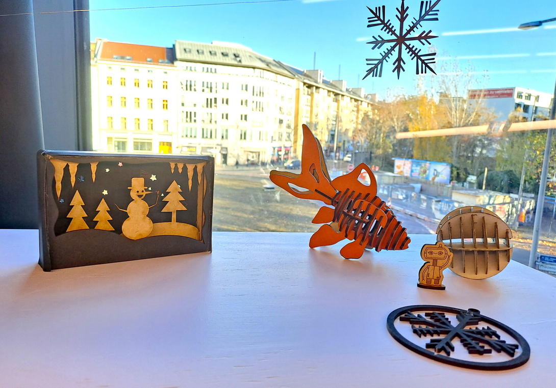 auf einem Tisch vor einem Fenster stehen Objekte aus dem Lasercutter, ein kleines Winter Panorama, ein roter Fisch, ein Sternschmuck für das Fenster etc.