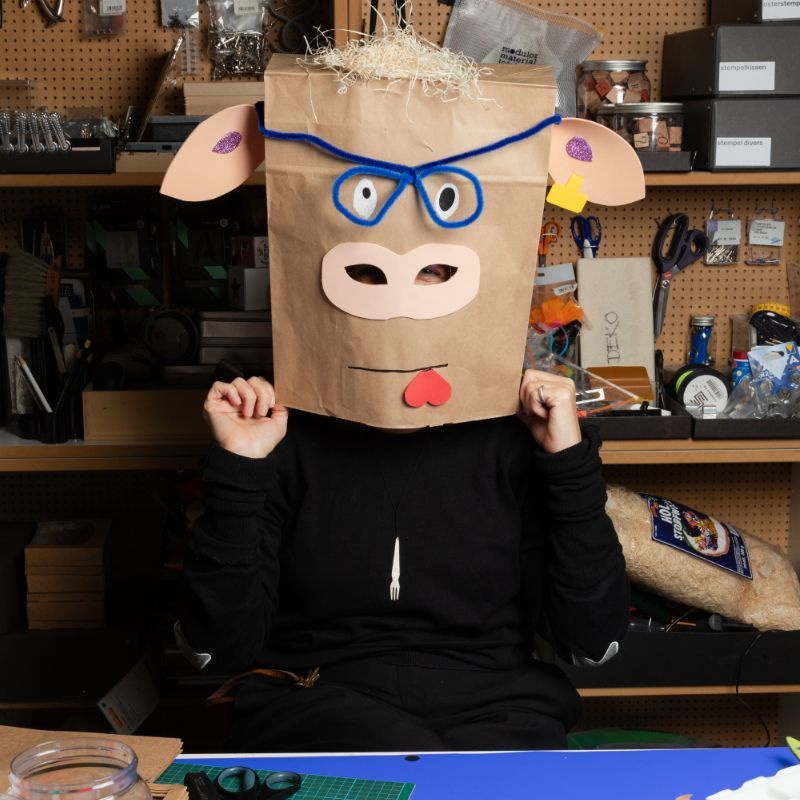 Mensch mit einer Schweinemaske, die aus einer oben und unten geöffneten braunen Papiertüte besteht