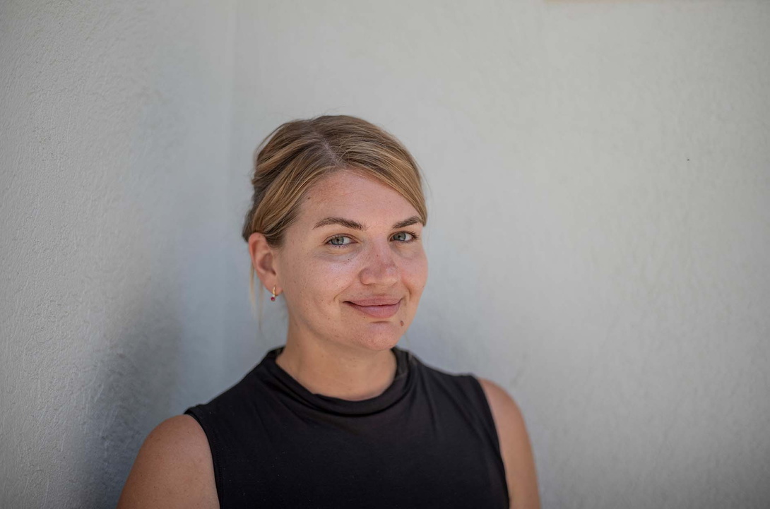 Porträt einer jungen weißen Frau mit zurückgebundenen blonden Haaren im ärmellosen dunklen Top vor weißer Wand