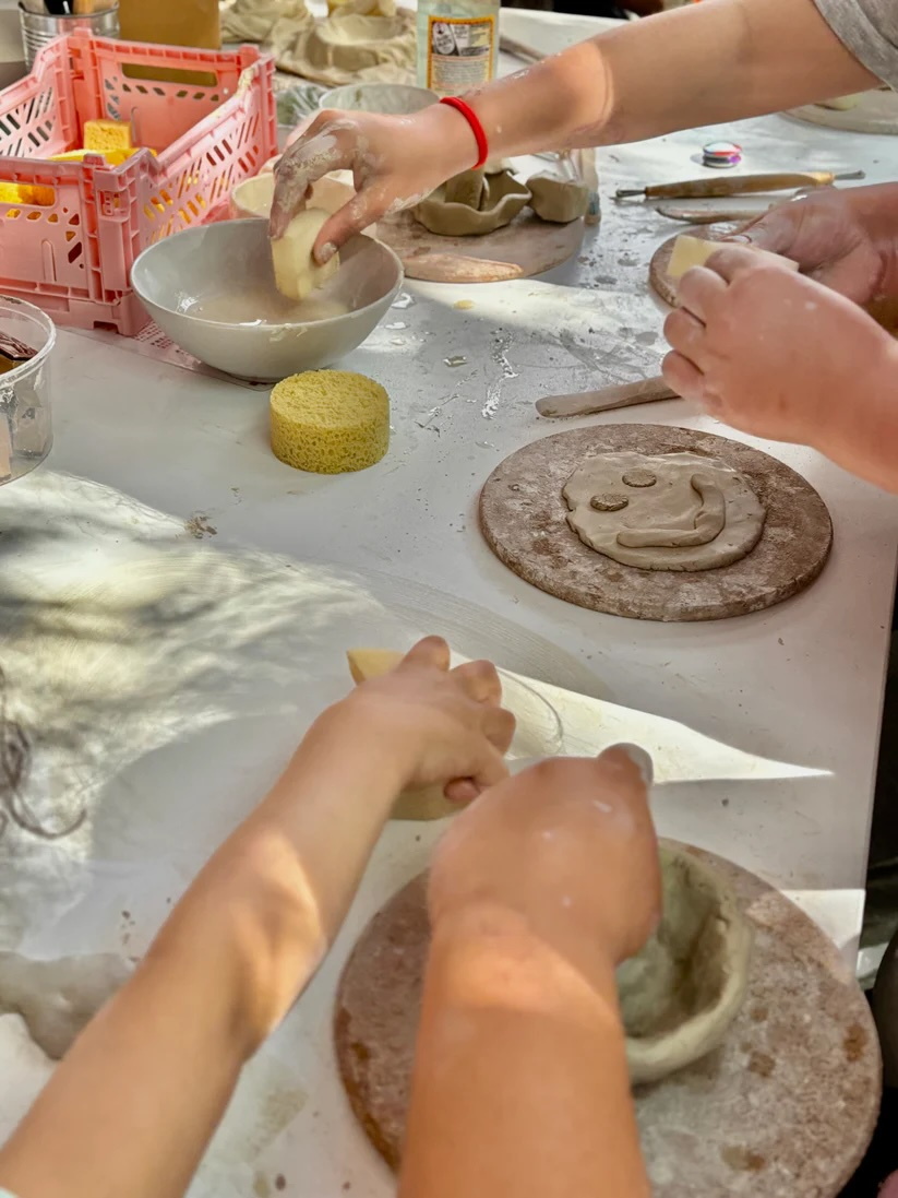 Kinderhände arbeiten mit Ton und Schwämmen mit Wasser an einem weißen Tisch