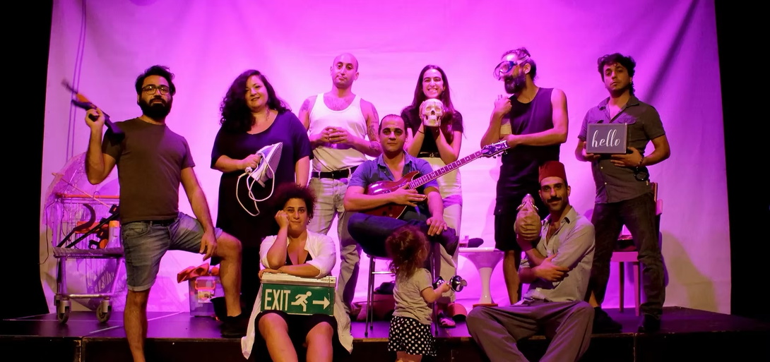 Gruppe Menschen mit Instrumenten auf einer Bühne, lila ausgeleuchtet