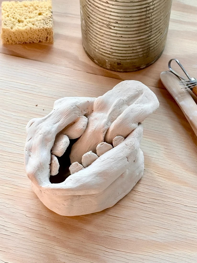 kleine Tonskulptur, ein geöffneter Mund mit Zähnen und großer Zunge, naturton-farben