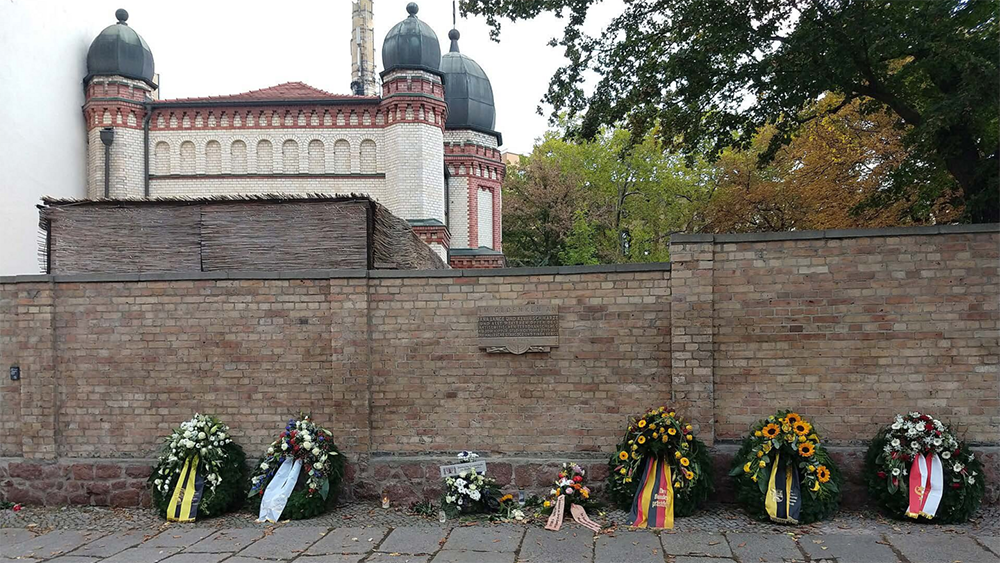 an einer Mauer liegen mehrere Blumenkränze zum Gedenken